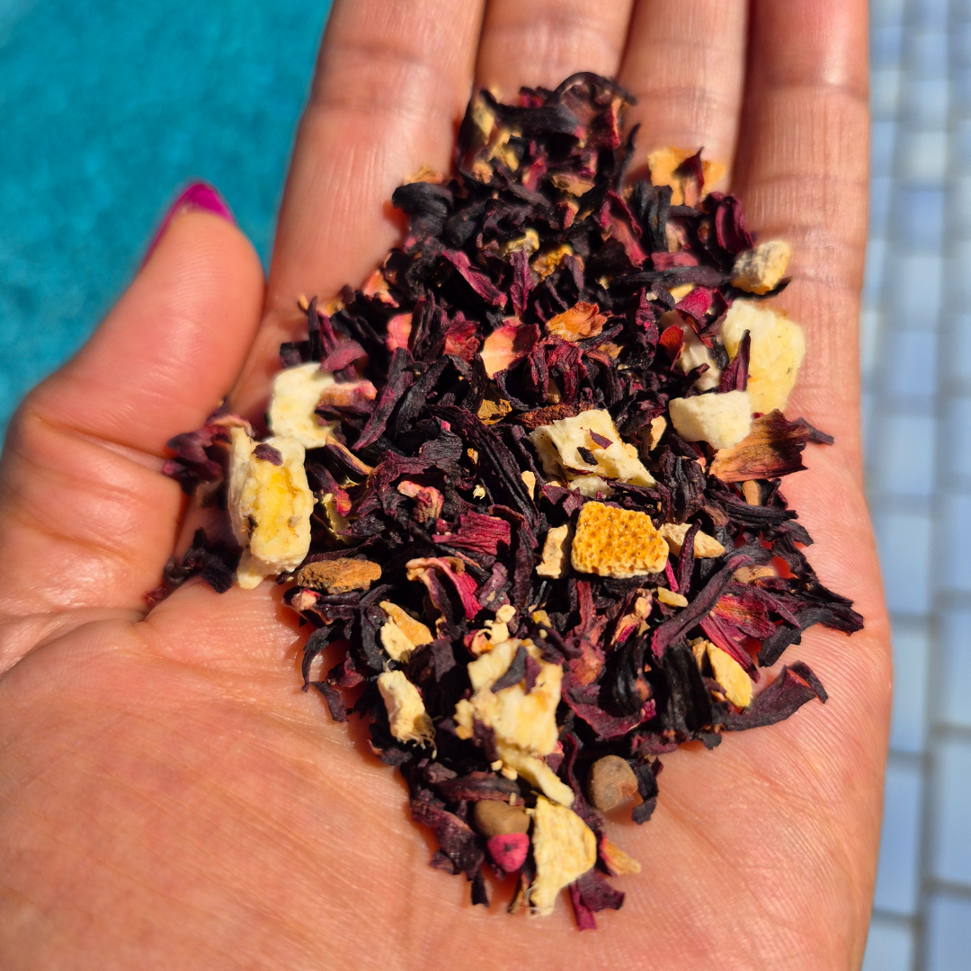 Hand holding a variety of dried tea leaves against a blue tiled wall. Zobo Joy